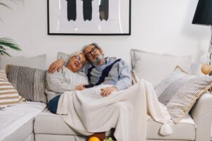 senior couple sitting close together on a sofa under blanket