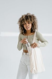 young woman in a casual outfit putting a bottle into a tote bag