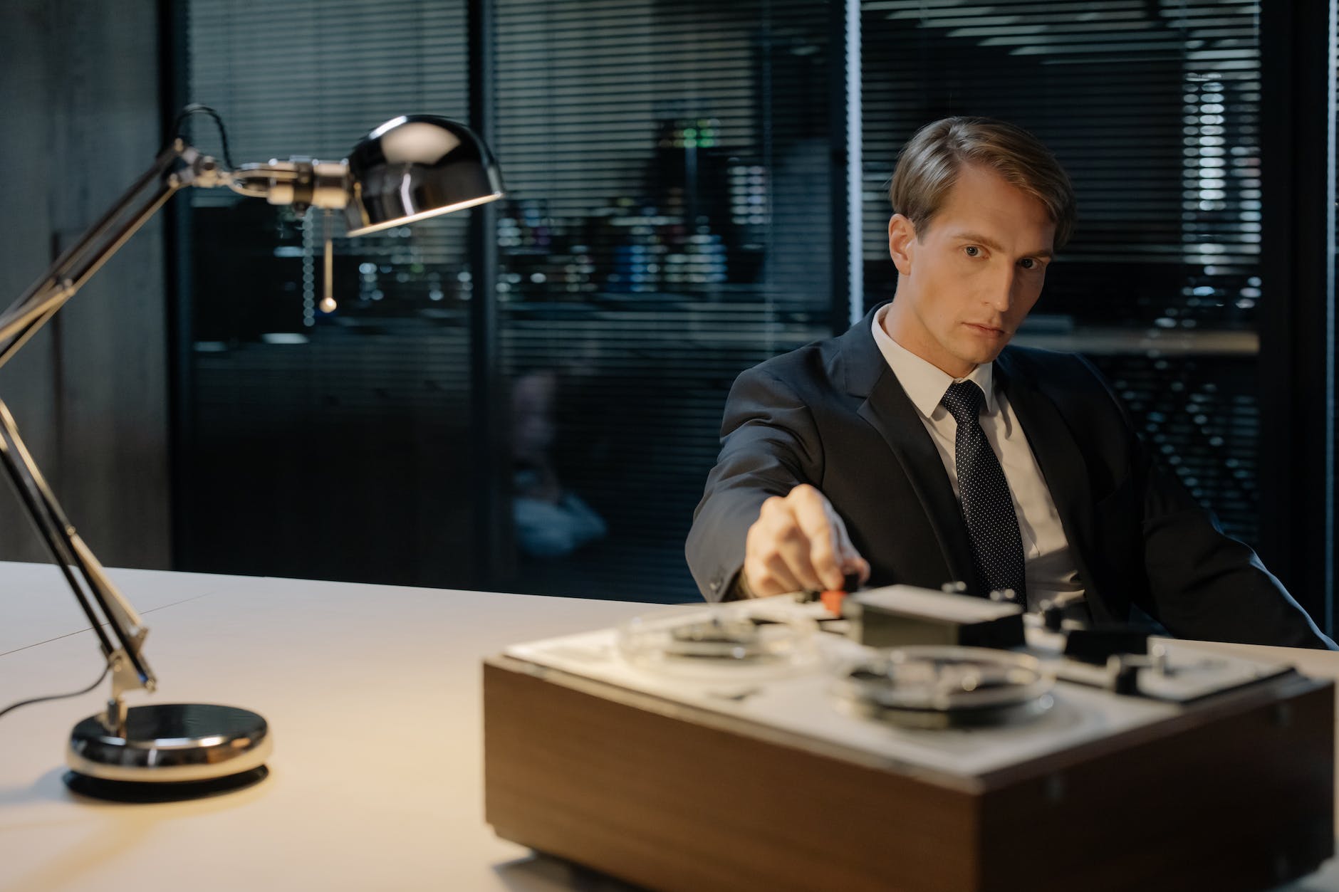 detective sitting at the desk with a reel to reel audio tape recorder