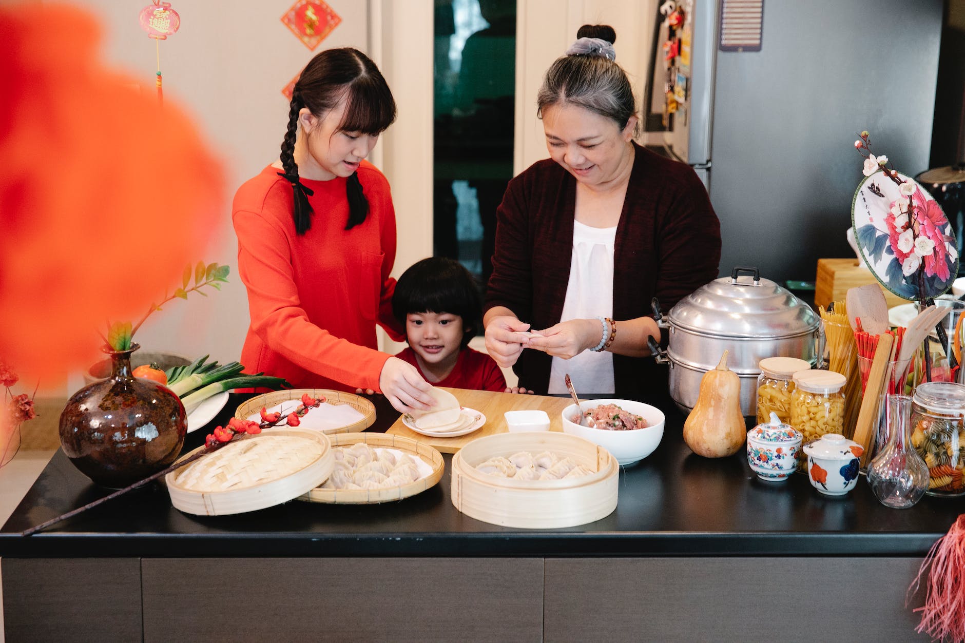 cheerful asian grandmother with teen and boy preparing dumplings